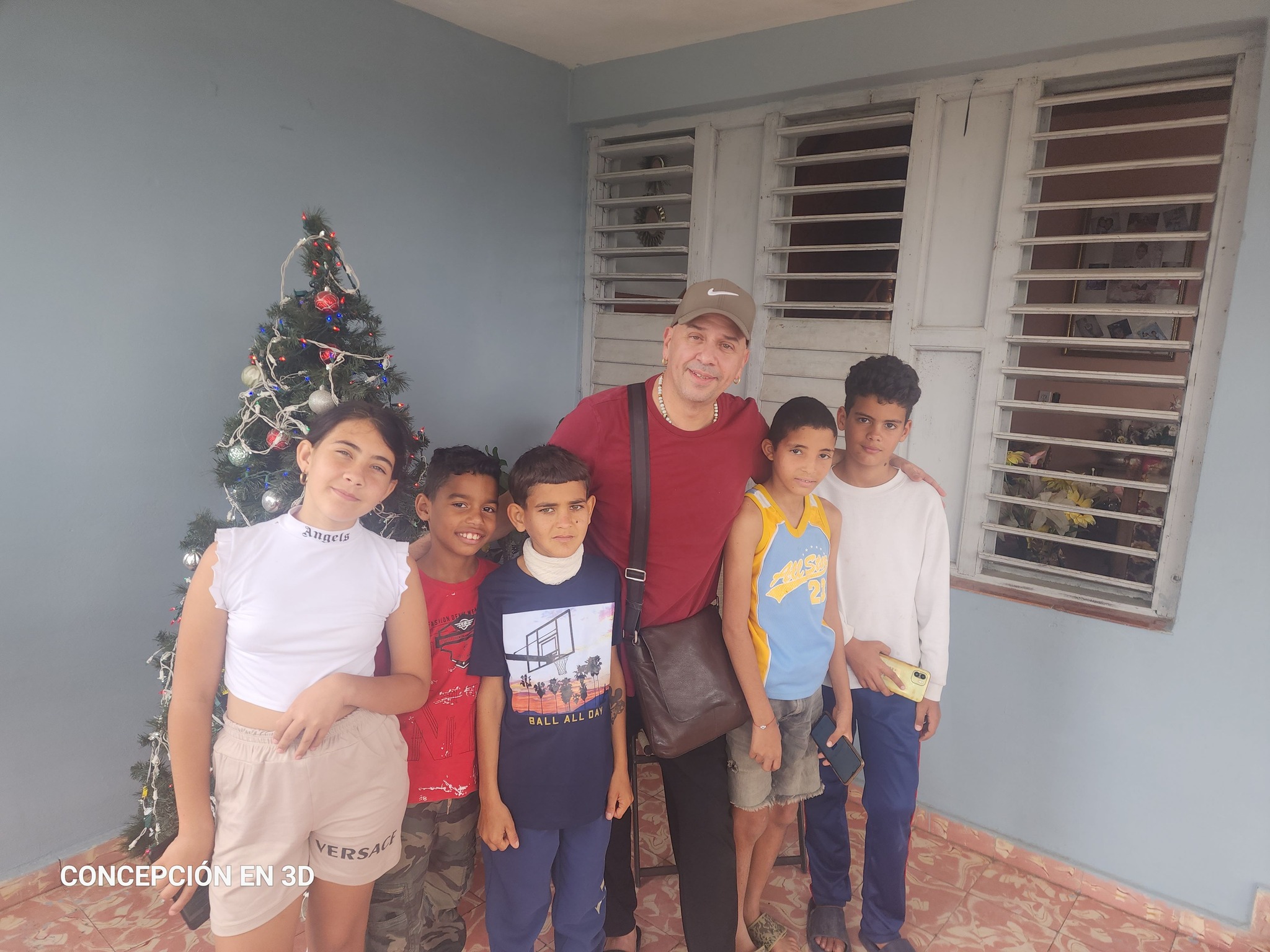Hombre adulto y niños sonriendo junto a árbol navideño
