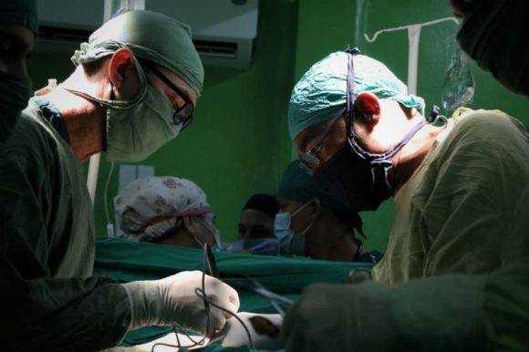 Cirujanos operando paciente en quirófano iluminado