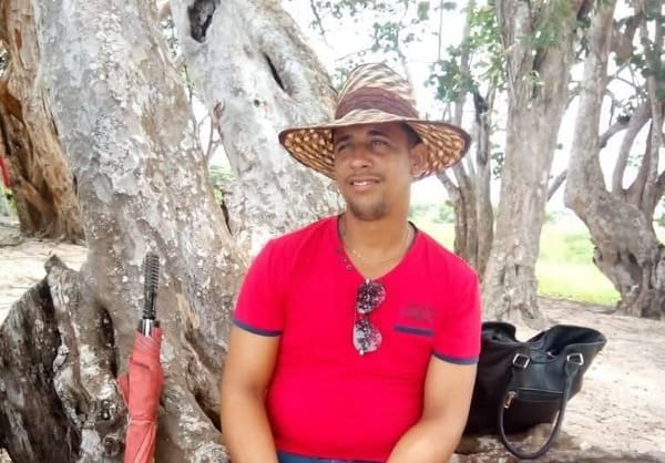 Hombre sonriente con sombrero sentado junto a árbol