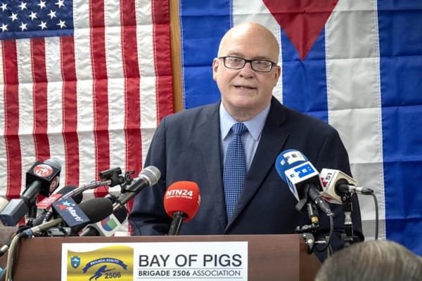 Hombre hablando en un podio con banderas de fondo