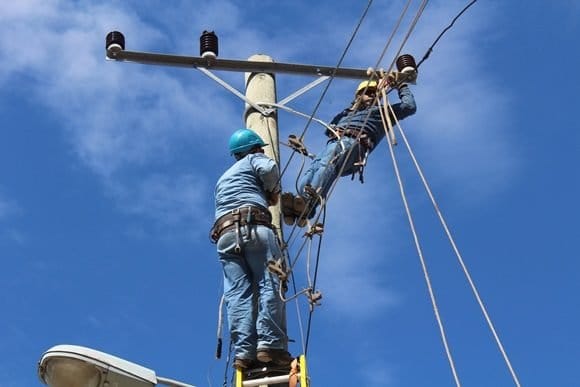 Técnicos reparando líneas eléctricas en poste alto