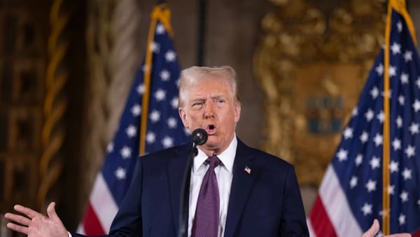 Hombre hablando en micrófono con banderas detrás