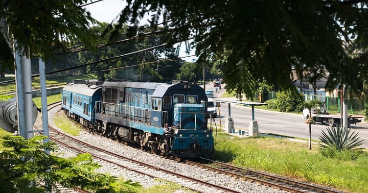 Tren azul en vía férrea, paisaje urbano.