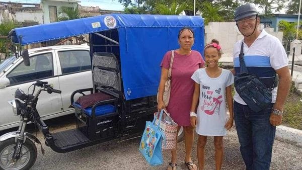 Familia frente a mototaxi azul en la calle.