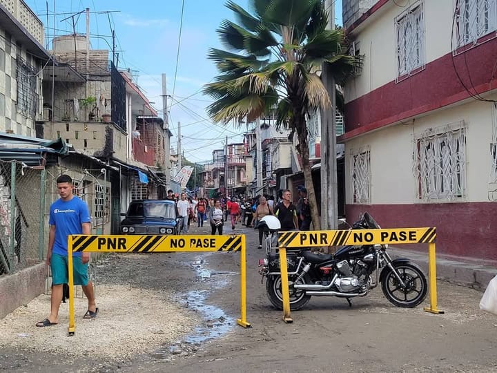 Barricada policial en calle con personas y vehículos.
