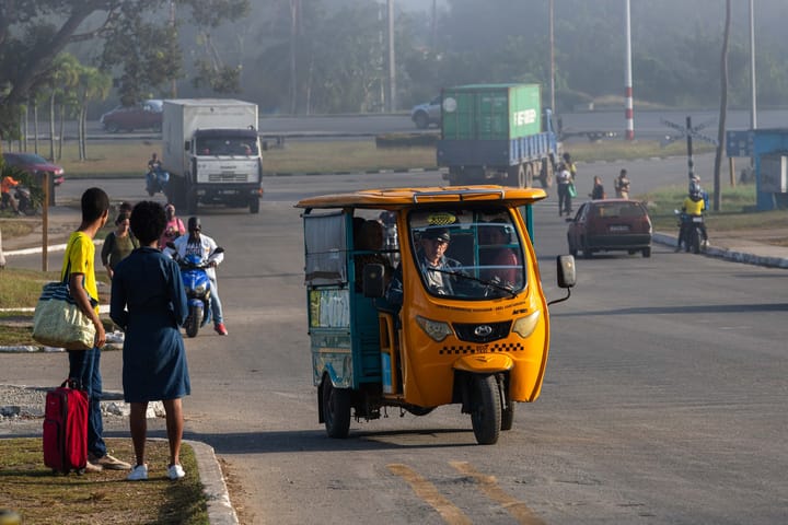 Mototaxi amarillo en carretera transitada con personas.