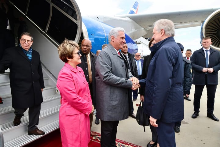 Líderes políticos se saludan en aeropuerto con gente alrededor.