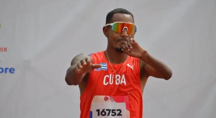 Atleta cubano en uniforme rojo, corriendo en carrera.