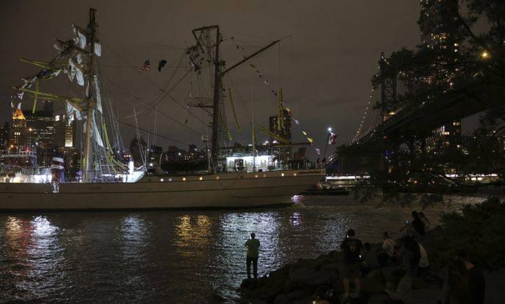 Velero iluminado en río nocturno junto a ciudad.