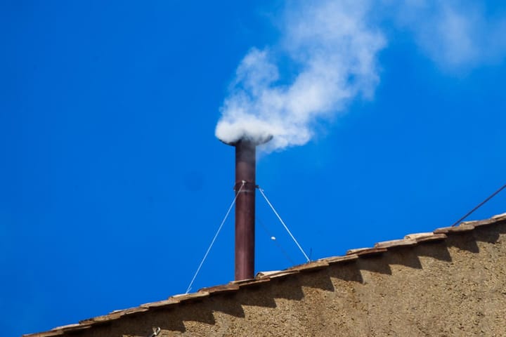 Humo blanco saliendo de una chimenea bajo cielo azul.