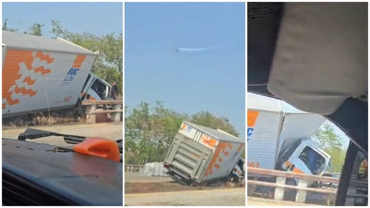 Accidente de camión en carretera, inclinado sobre barandilla.