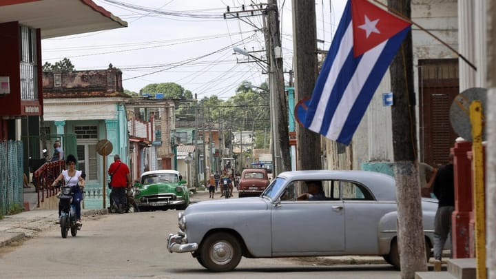 Calle en Cuba con coches clásicos y bandera cubana.