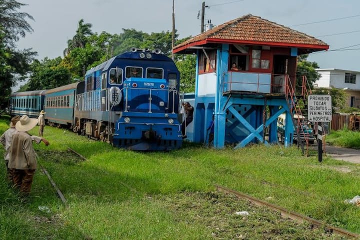 Tren azul pasando por una estación rural con señal.