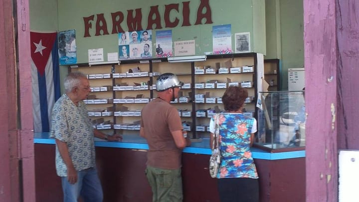 Personas esperando en farmacia con estantes de medicinas