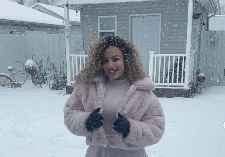Mujer sonriente bajo nieve con abrigo rosa
