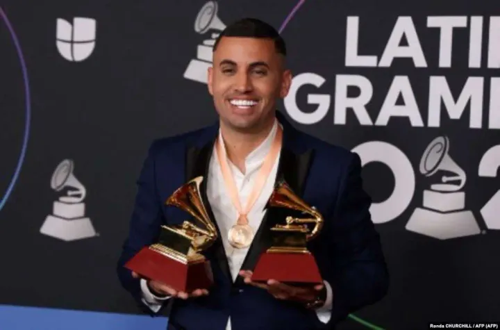 Hombre sonriente sostiene dos premios Grammy