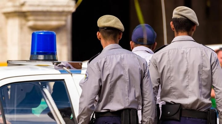 Policías junto a un coche patrulla con luces.
